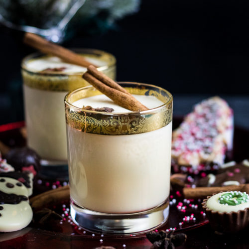 Bourbon Eggnog on a cookie and candy plate in gold rimmed glasses garnished with star anise and cinnamon