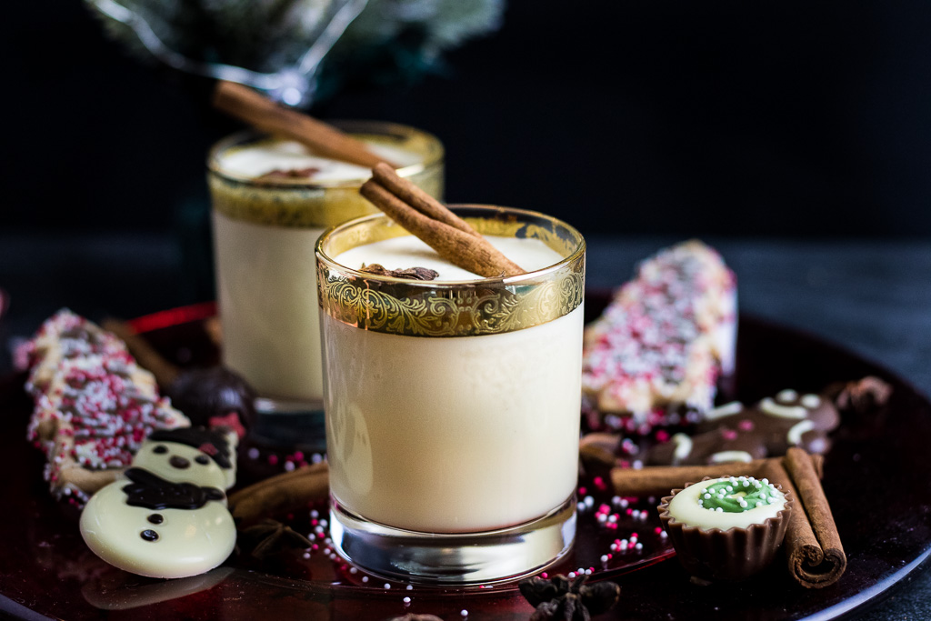 Bourbon Eggnog on a cookie and candy plate in gold rimmed glasses garnished with star anise and cinnamon