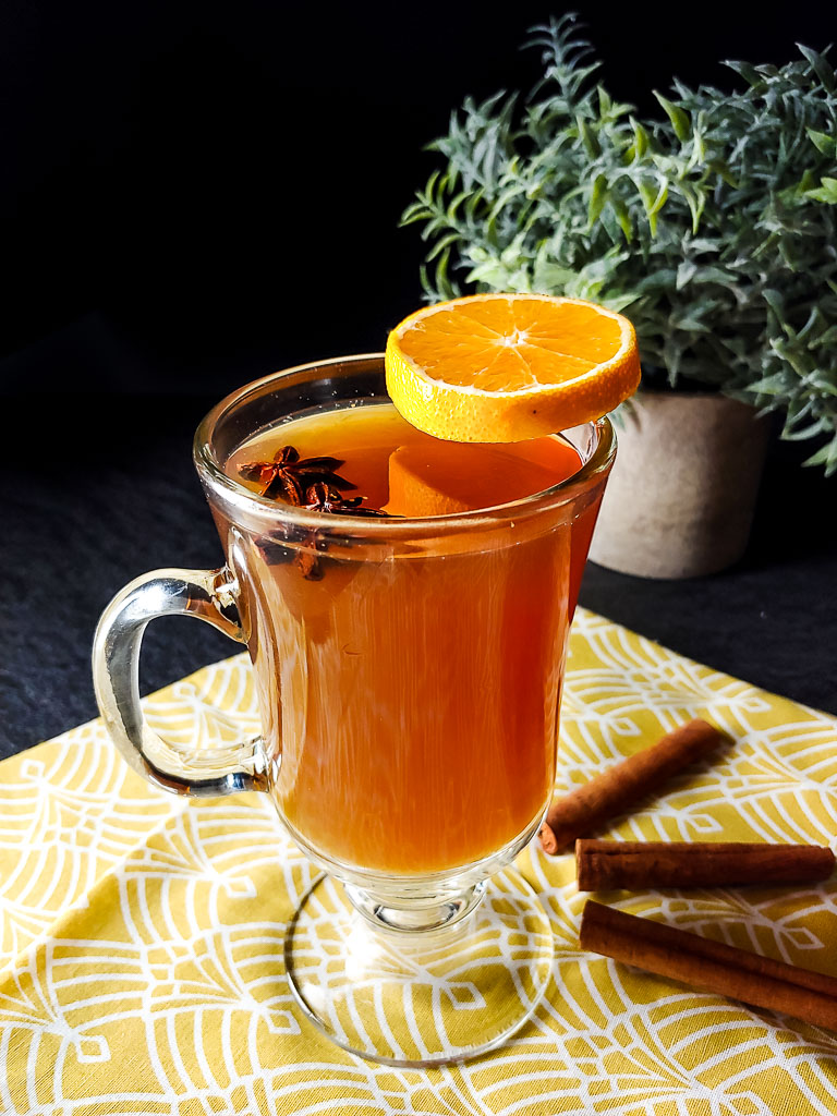 Bourbon and beer toddy in a clear mug with a cream float and orange wheel garnish