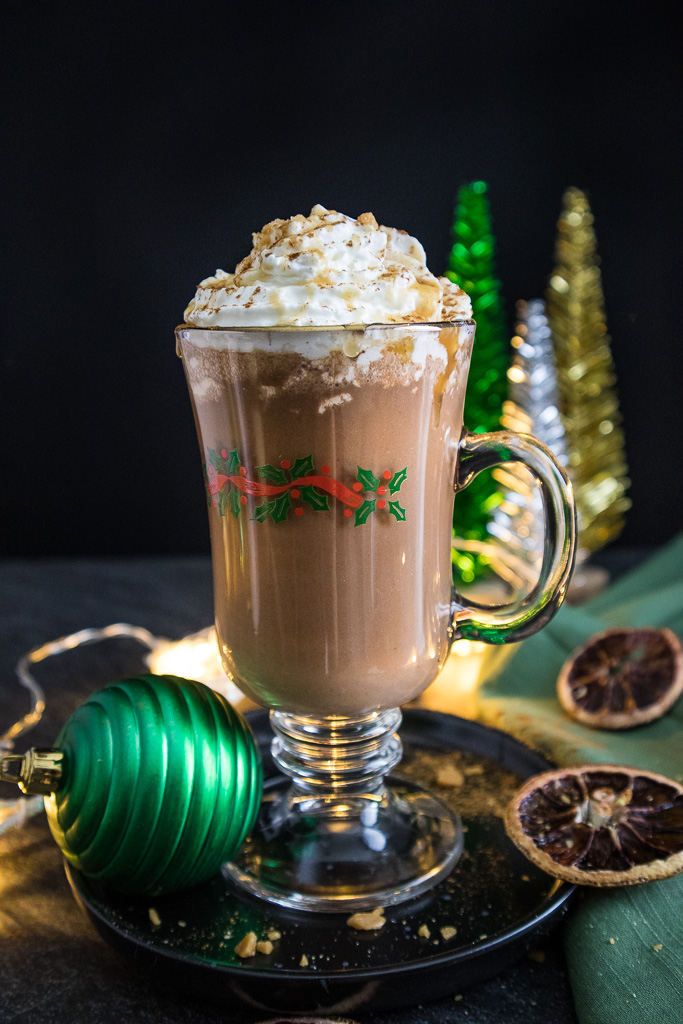 Caramel Orange Hot Chocolate topped with whipped cream and caramel drizzle on a plate with christmas lights and ornaments