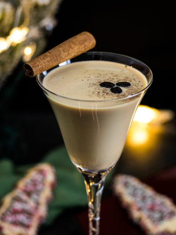 Eggnog Espresso Martini with cinnamon stick, fresh nutmeg and coffee beans in a tall martini glass