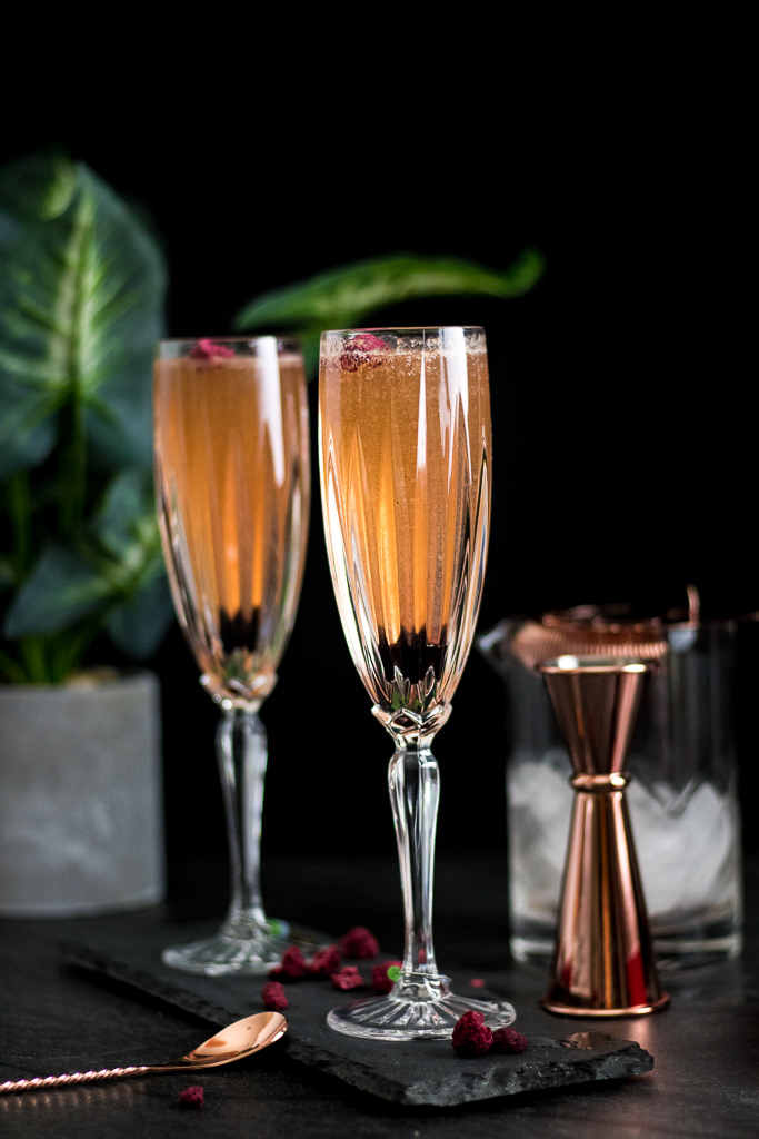 Raspberry Champagne Bubbles Cocktail in champagne flutes with copper-plated barware set and raspberry syrup and bitters