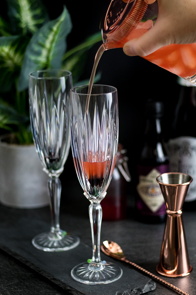 Raspberry Champagne Bubbles Cocktail in champagne flutes with copper-plated barware set and raspberry syrup and bitters