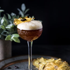Carajillo in a tall coupe with dried pineapple slice and coffee beans