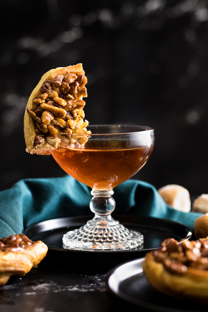 Pecan Sticky Bun Cocktail in a coupe glass garnished with pecan sticky bun quarter