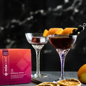 Two Smoked Cherry Manhattans with Mixcles package box nearby, garnished with orange peel