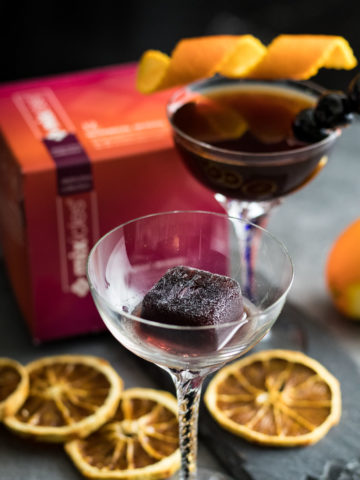 Two Smoked Cherry Manhattans with Mixcles package box nearby, garnished with orange peel