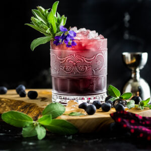 Blueberry Sage Julep in a frosted rocks glass with sage garnish, blueberries and violet garnish