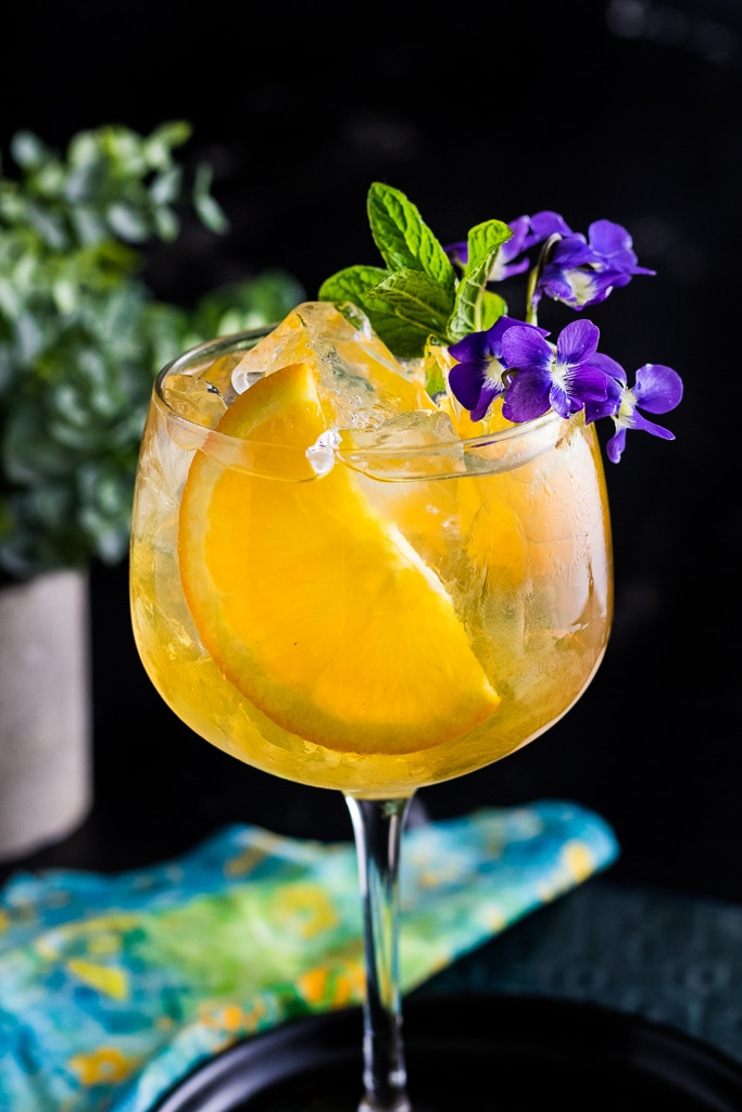 Spring Bourbon Spritz with orange slice and mint as garbage, served over ice in a large wine glass.