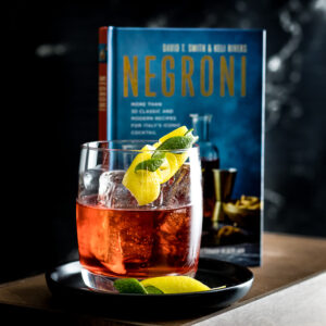 Oaxacan - a Negroni - Red cocktail on the rocks with lemon and lime peel and Negroni book in background