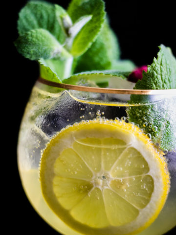 Limoncello Spritz in a wine glass with ice garnished with mint and lemon wheel, flowers