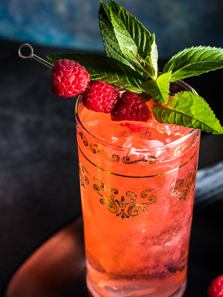 Raspberry Bourbon Buck cocktail in a tall collins glass with ice garnished with raspberries and min