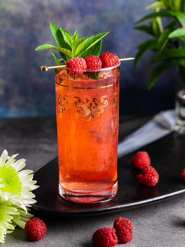 Raspberry Bourbon Buck cocktail in a tall collins glass with ice garnished with raspberries and mint