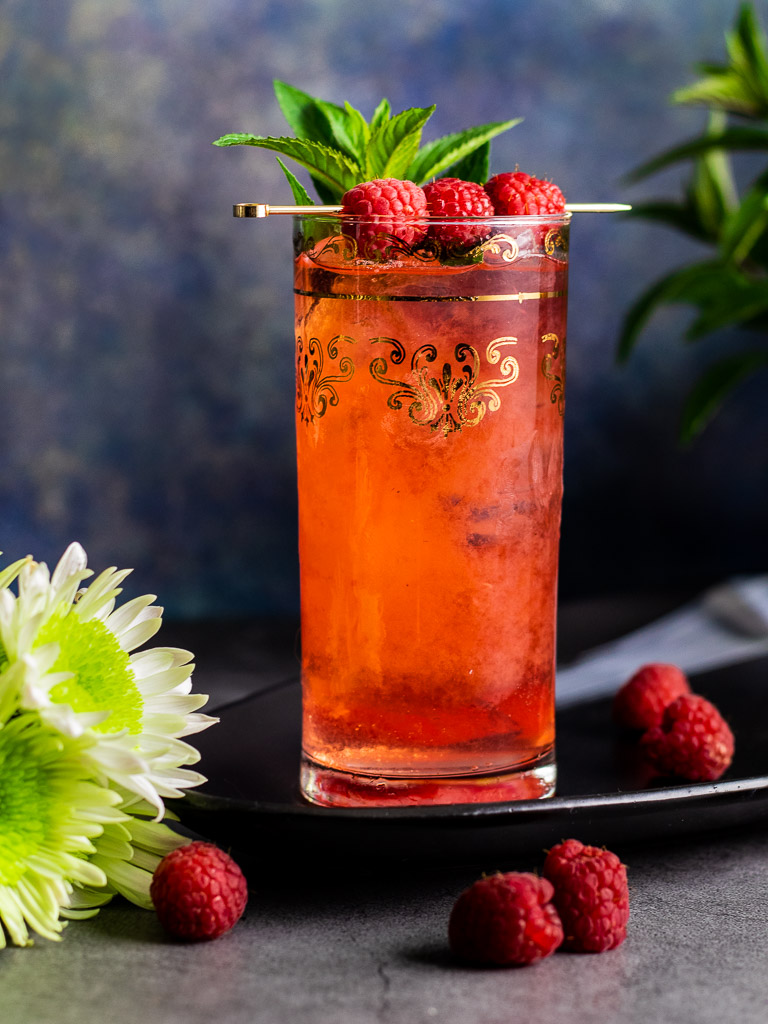 Raspberry bourbon and ginger cocktail in a tall glass garnished with fresh raspberries and mint