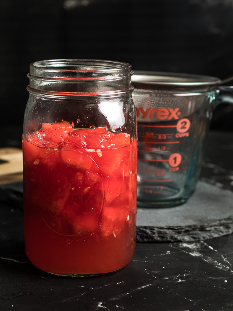 Watermelon Syrup for Cocktails - A jar ready to be strained next to a measuring cup with strainer.