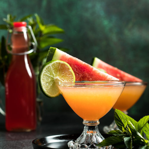 Watermelon Whiskey Cocktail in two coupe glasses garnished with a spear of watermelon and lime wheel