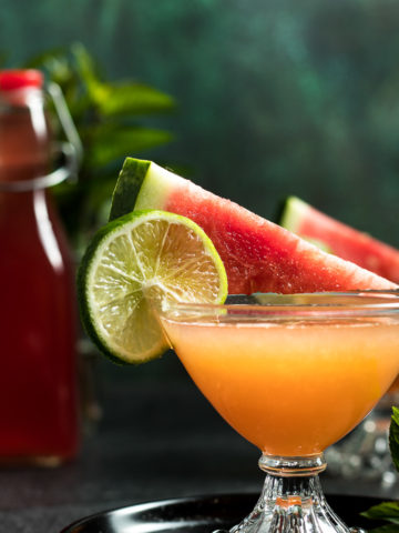Watermelon Whiskey Cocktail in two coupe glasses garnished with a spear of watermelon and lime wheel