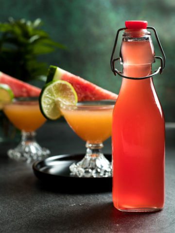 watermelon syrup in a jar with two whiskey watermelon sour cocktails