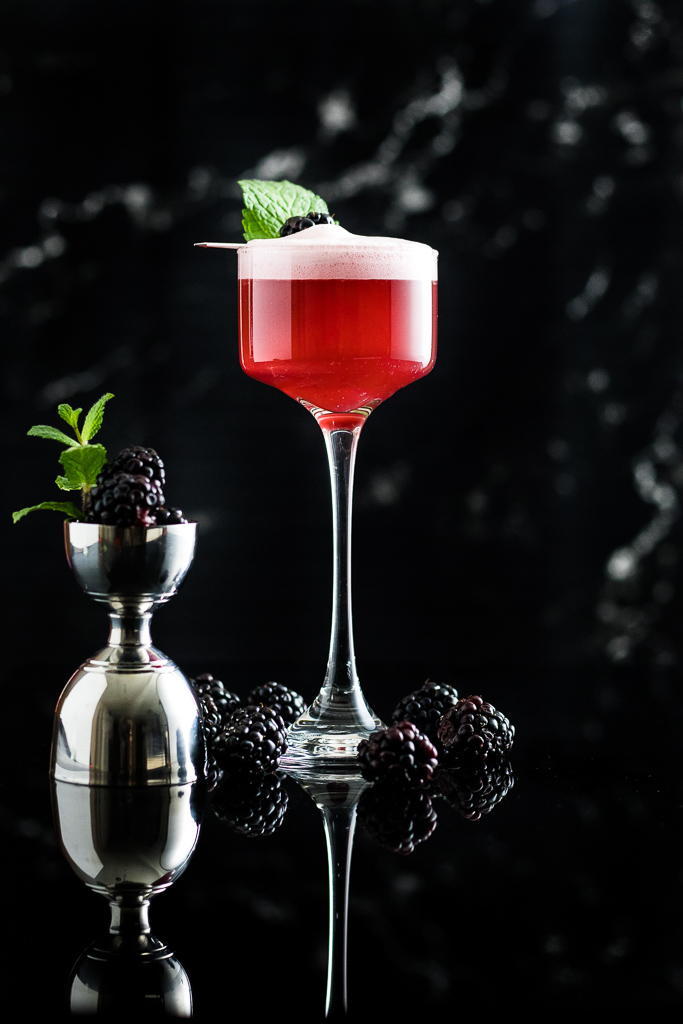 blackberry whiskey sour with foam and blackberry garnish in a coupe glass