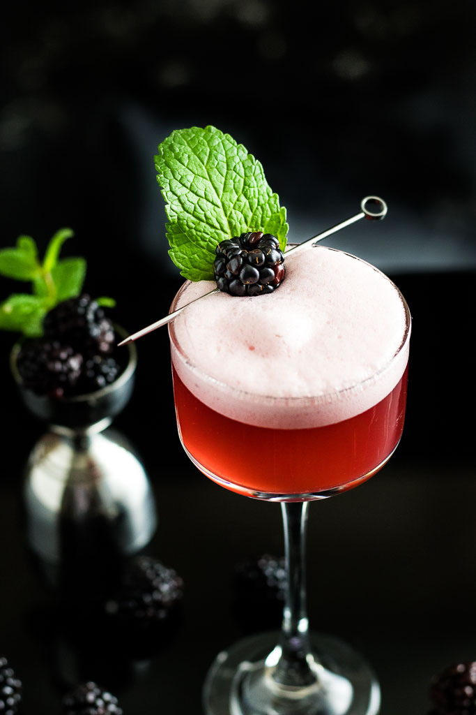 blackberry whiskey sour with foam and blackbery garnish in a coupe glass