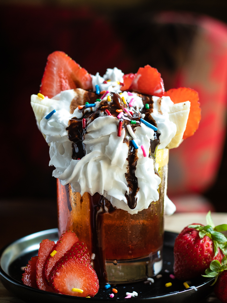 Banana Boulevardier with banana, whipped cream, strawberries and chocolate drizzle on top