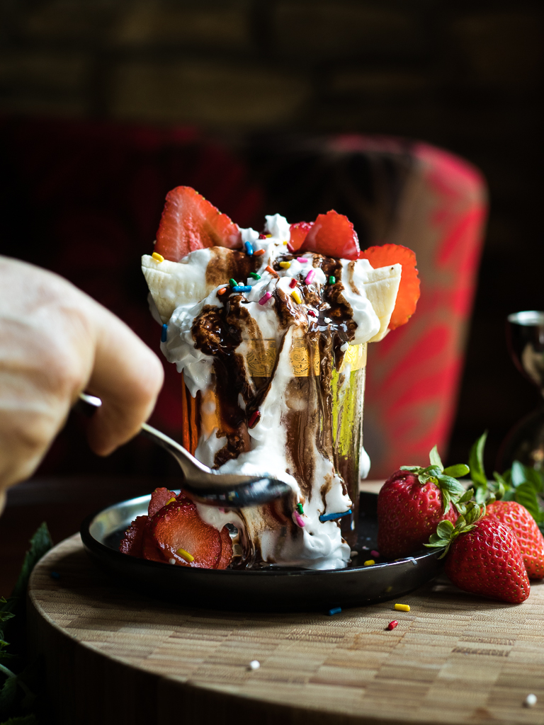 Banana Boulevardier with banana, whipped cream, strawberries and chocolate drizzle on top