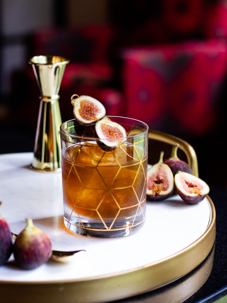 Fig Old Fashioned on a tray with fresh figs and jigger, garnished with fresh fig