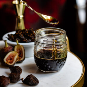 Homemade Fig Syrup in a jar with dried and fresh figs on a tray
