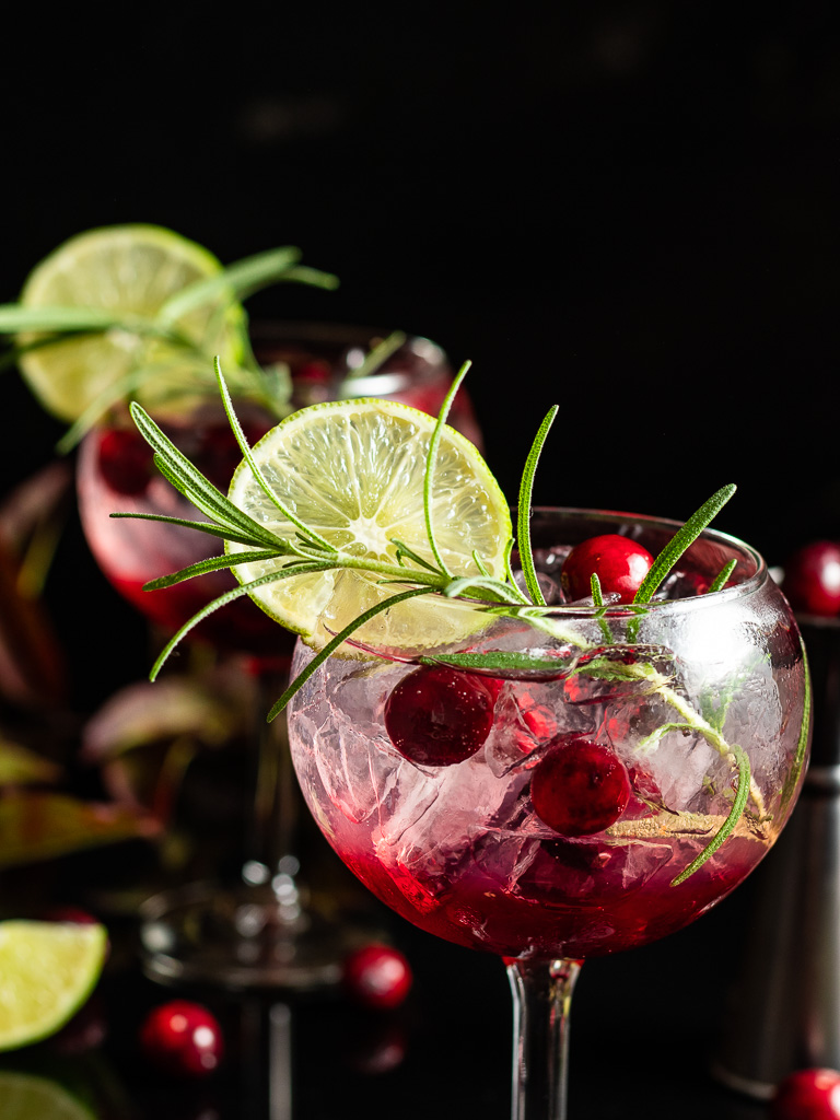cranberry gin and tonic in a balloon glass with rosemary and cranberry garnish