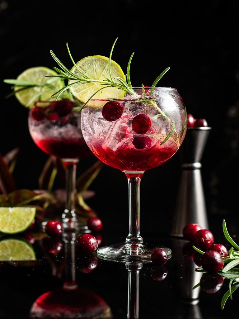 cranberry gin and tonic in a balloon glass with rosemary and cranberry garnish