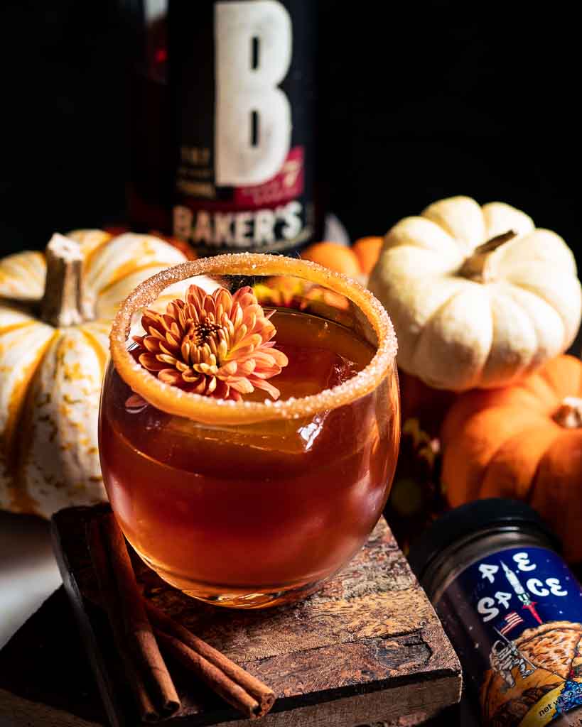 Thanksgiving Pumpkin Spice Cocktail Old Fashioned with flower garnish, caramel rim and Bakers bourbon in background