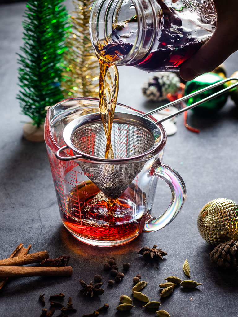 Christmas Mulled Vermouth with mulled spice in a jar with sweet vermouth and loose spices in the background