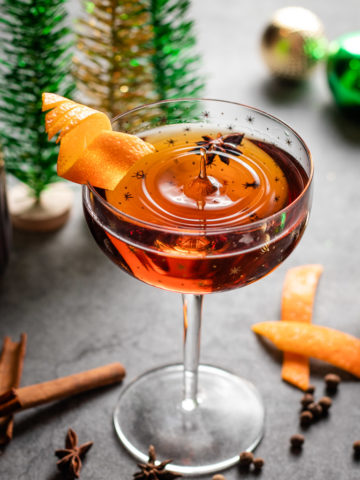Christmas Manhattan cocktail with orange garnish and star anise with spices around it