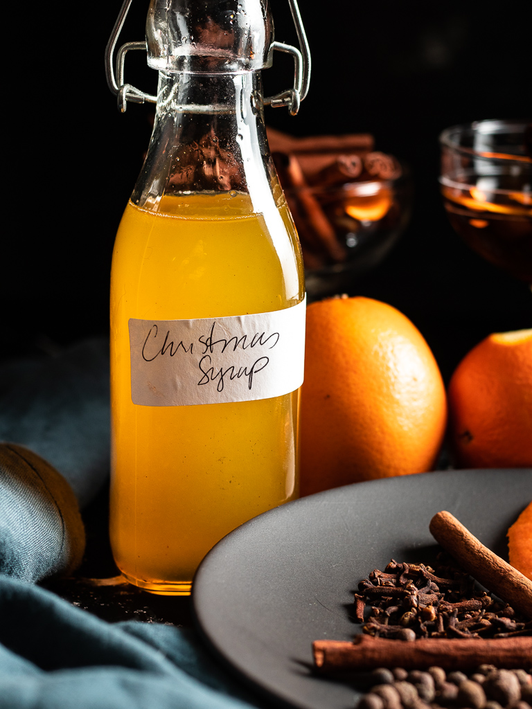 Christmas Syrup in a small glass bottle with spices and oranges on a plate
