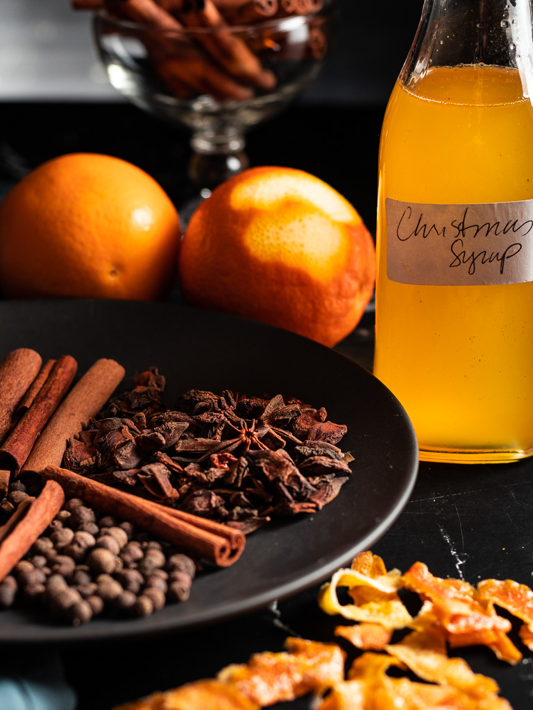 Christmas Syrup in a small glass bottle with spices and oranges on a plate