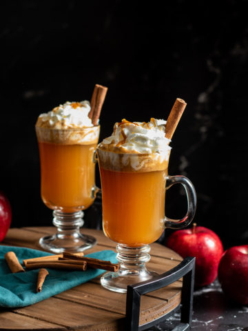 Hot Buttered Cider in a mug topped with whipped cream and a cinnamon stick