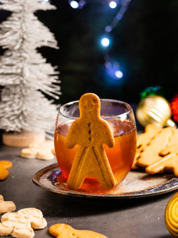 gingerbread old fashioned cocktail on a silver tray with cookies and oranments in the background.