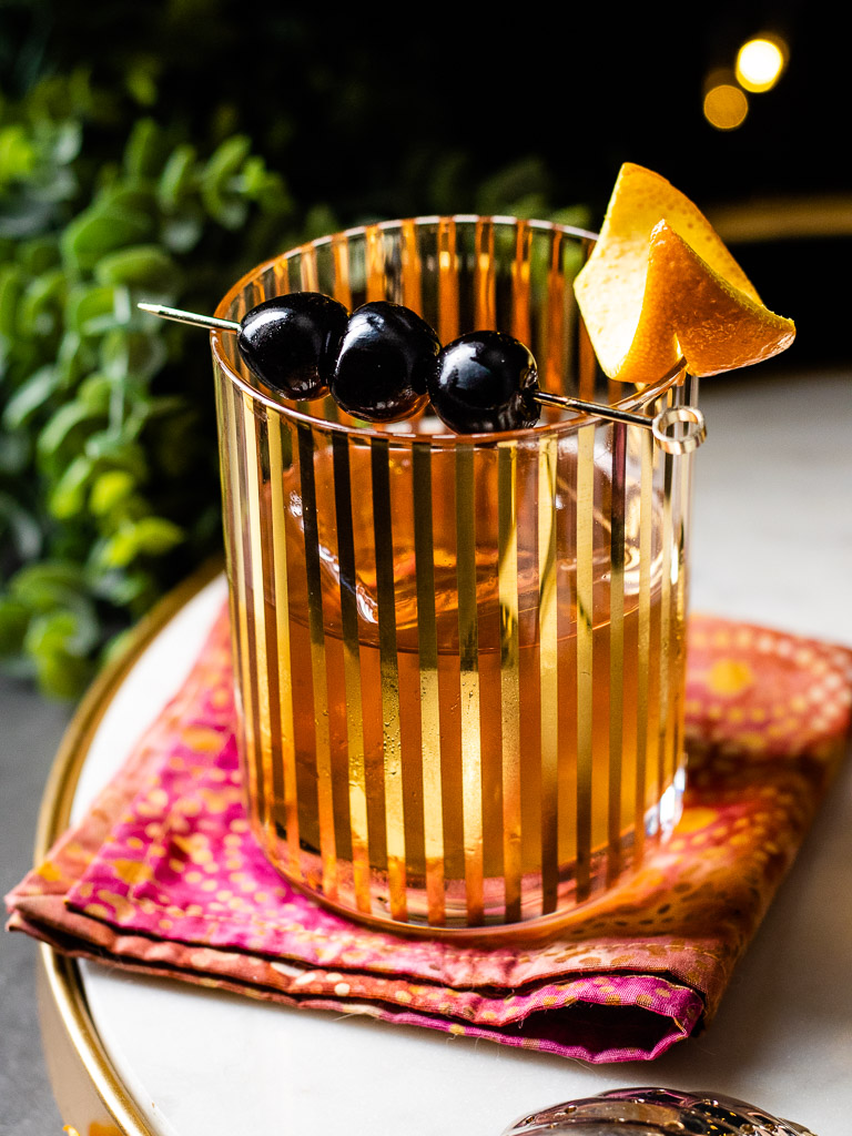 Sherry Old Fashioned in a gold accent glass with orange peel and cherries