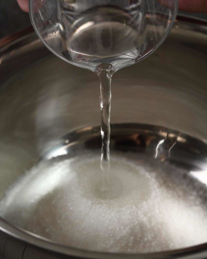 water being poured onto sugar in a pan