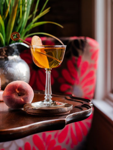 Peach Manhattan in a coupe glass with a peach slice as garnish