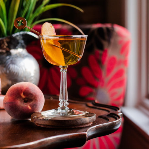 Peach Manhattan in a coupe glass with a peach slice as garnish