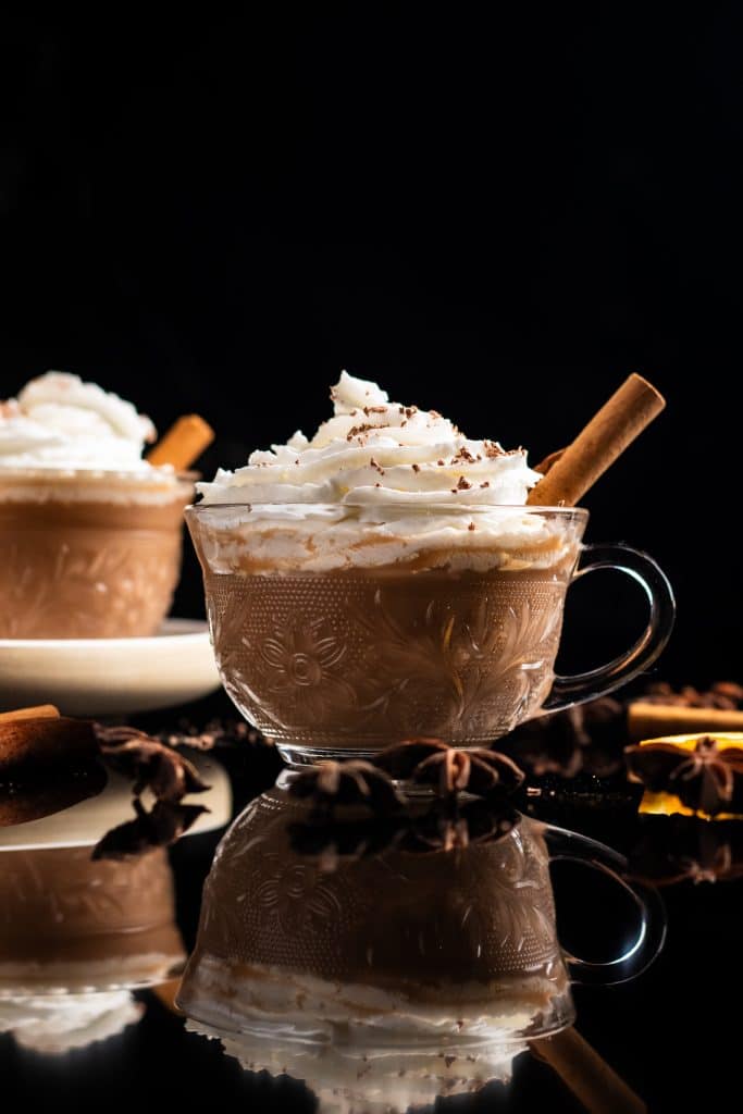 two cups of bourbon hot chai latte topped with whipped cream and cinnamon stick
