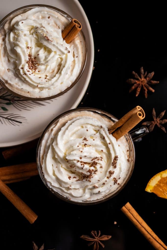 two cups of bourbon hot chai latte topped with whipped cream and cinnamon stick