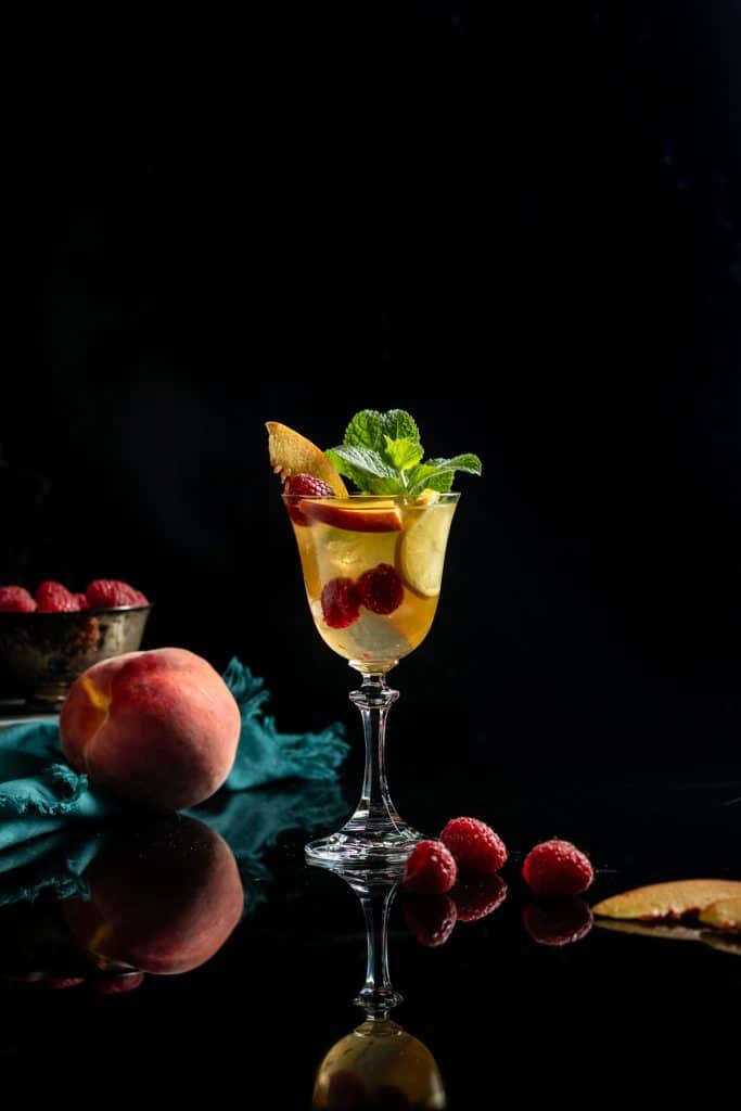 berry peach sangria in a wine glass with peaches and mint