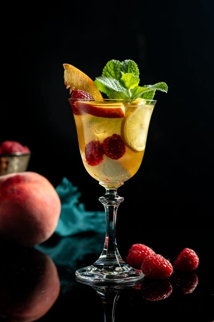 berry peach sangria in a wine glass with peaches and mint