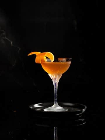 Orange marmalade Breakfast manhattan in a coupe class with an orange twist garnish on a small back plate against a black background