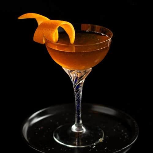 Orange marmalade Breakfast manhattan in a coupe class with an orange twist garnish on a small back plate against a black background